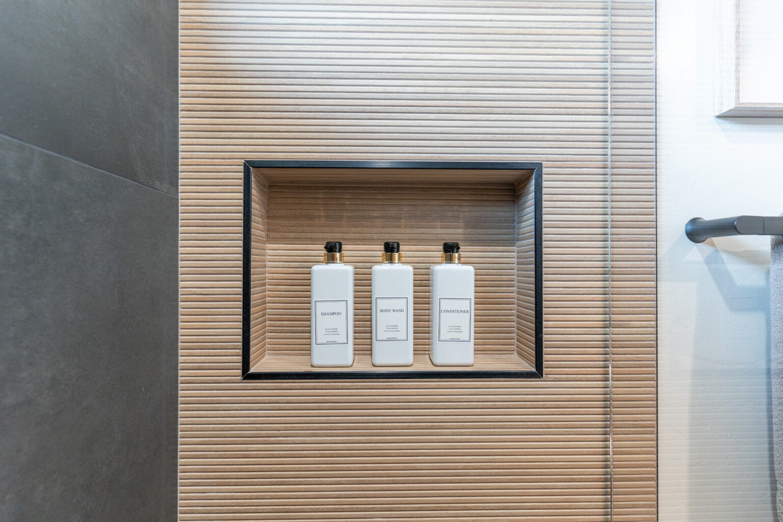 Modern walk-in shower with glass enclosure, custom tile floor, black fixtures, and wood-accented vanity by a San Diego bathroom remodeling contractor – Lusso Design and Build.